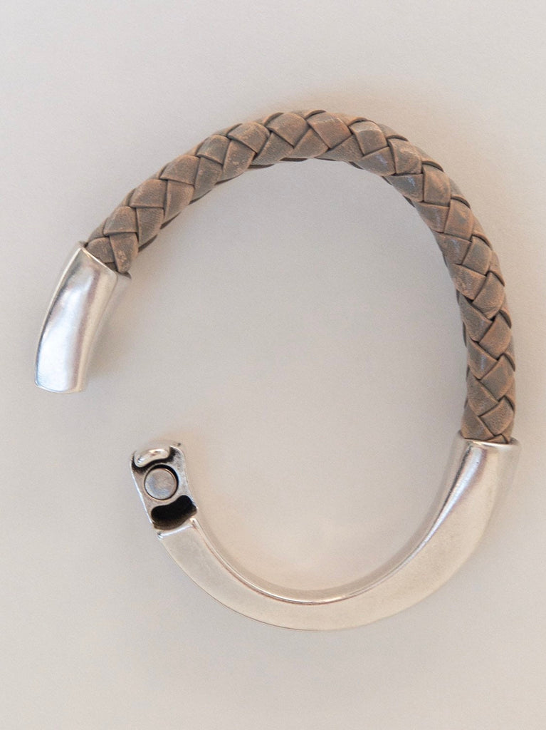 a gray braided leather bracelet with magnetic clasp sits on a white table with the clasp slightly open