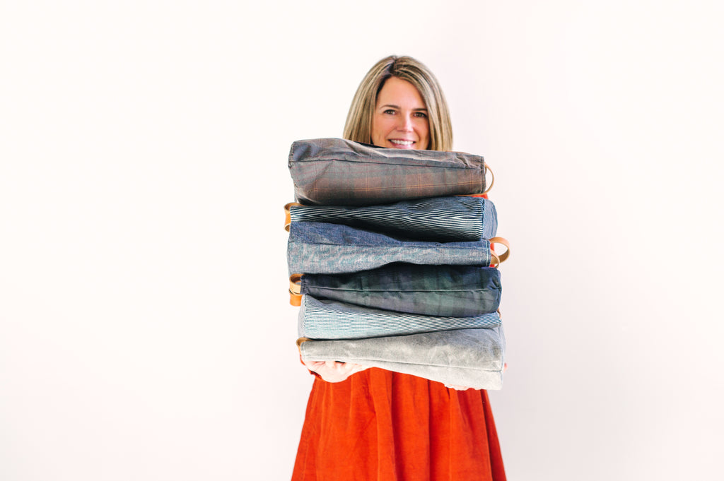 A woman smiles for the camera while holding a stack of waxed denim bags