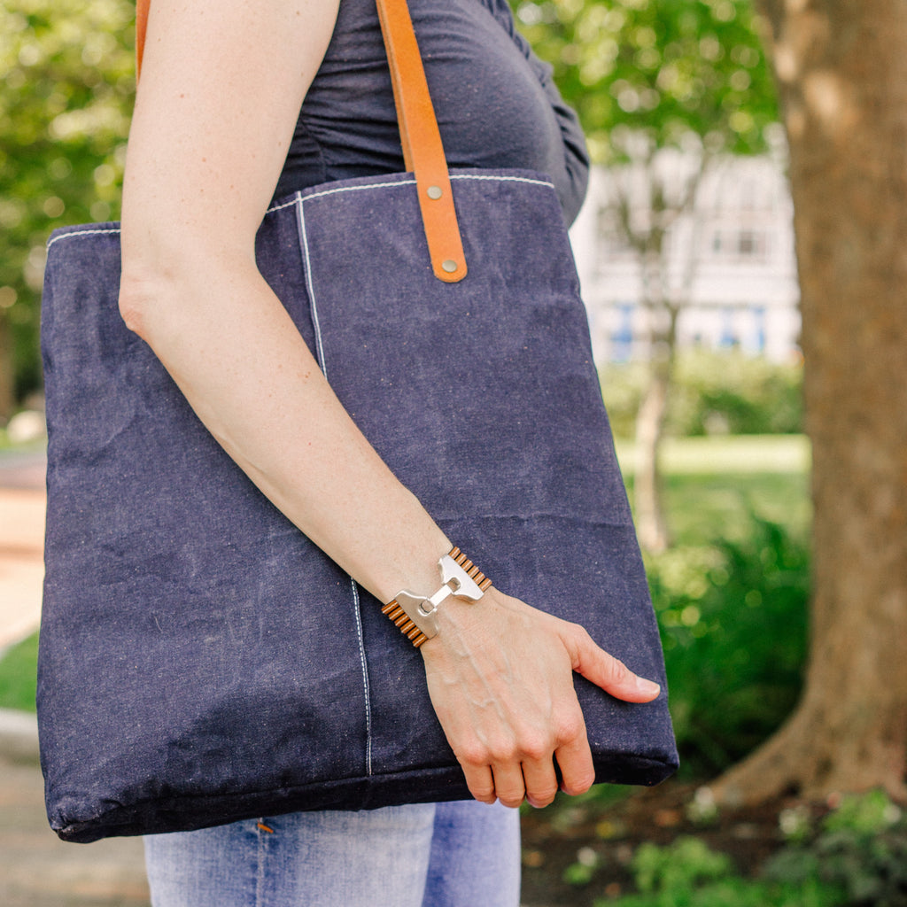 A woman holds a dark navy waxed denim bag with brown leather straps