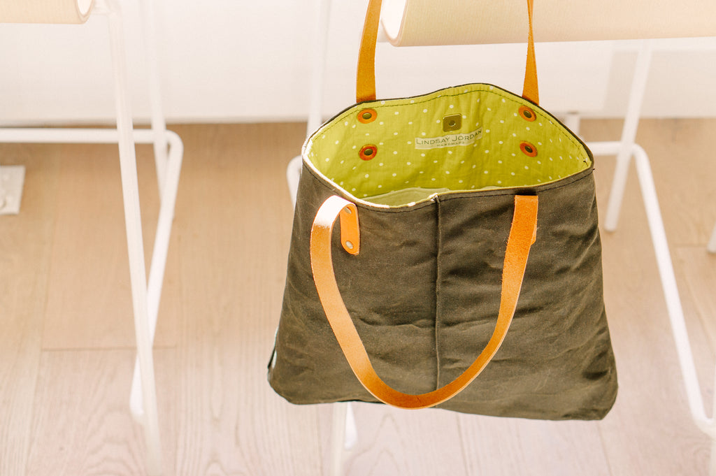 An army green waxed canvas bag with bright green polka dot lining hangs off a white chair