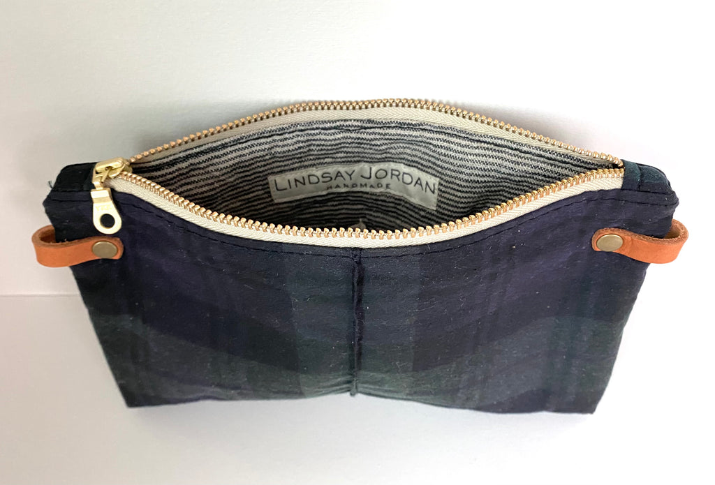 A blackwatch plaid wrist clutch is open to show a striped lining fabric