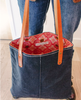 A dark blue waxed denim bag with brrown leather staps hands down to show a bright red fully lined inside pocket.