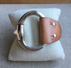 This large brown leather and Zamak snaffle bit bracelet is placed on a burlap pillow