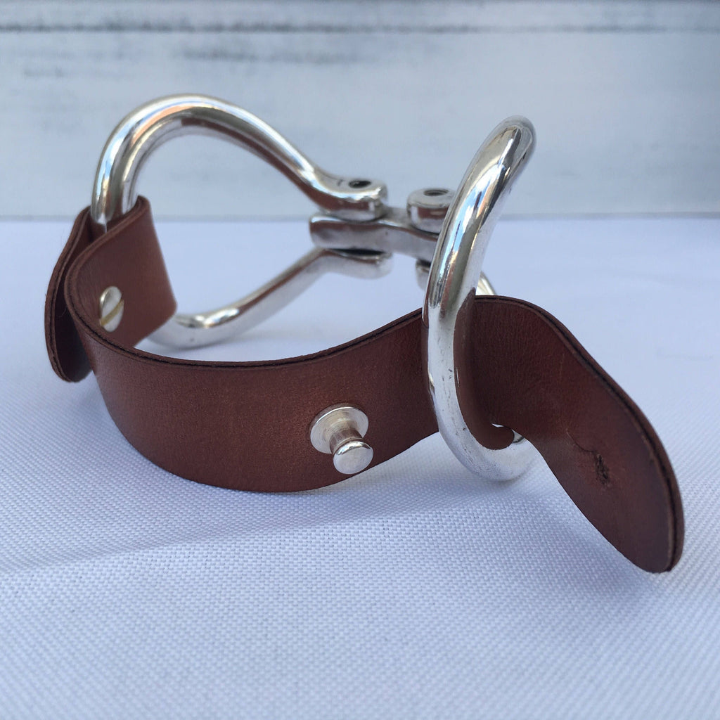 A two-sided Zamak snaffle bit bracelet sits on a white table unbuckled