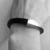 A thick black leather bracelet with silver clasp on a woman's wrist