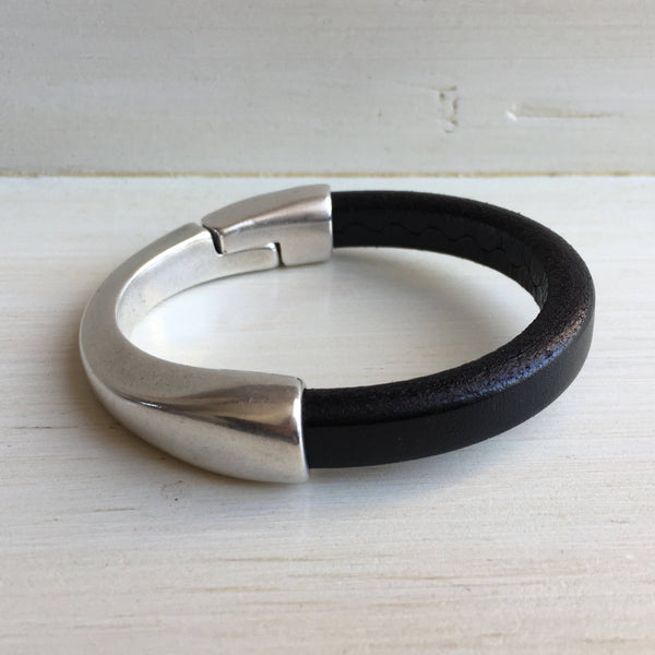 a thick black leather bracelet with silver clasp on a white table