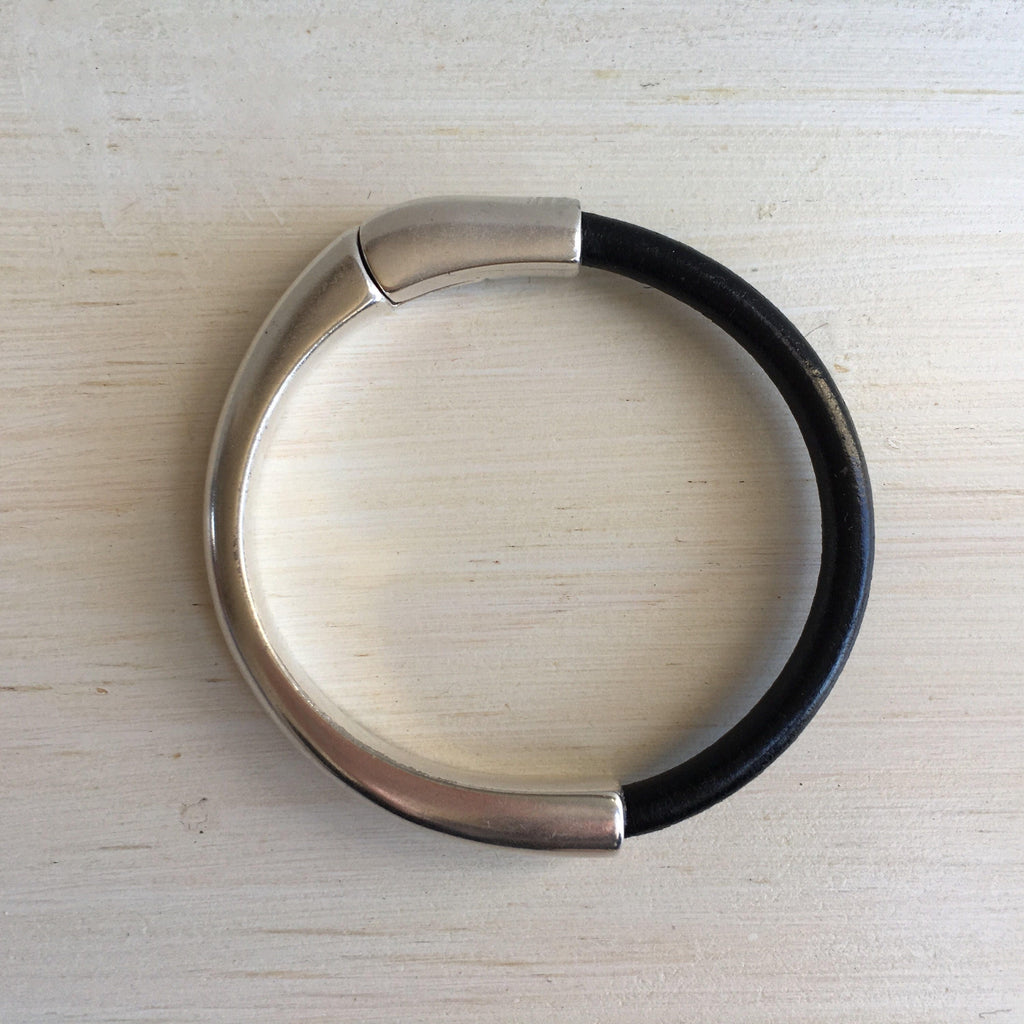 a black leather bracelet with silver magnetic clasp sits on a white table