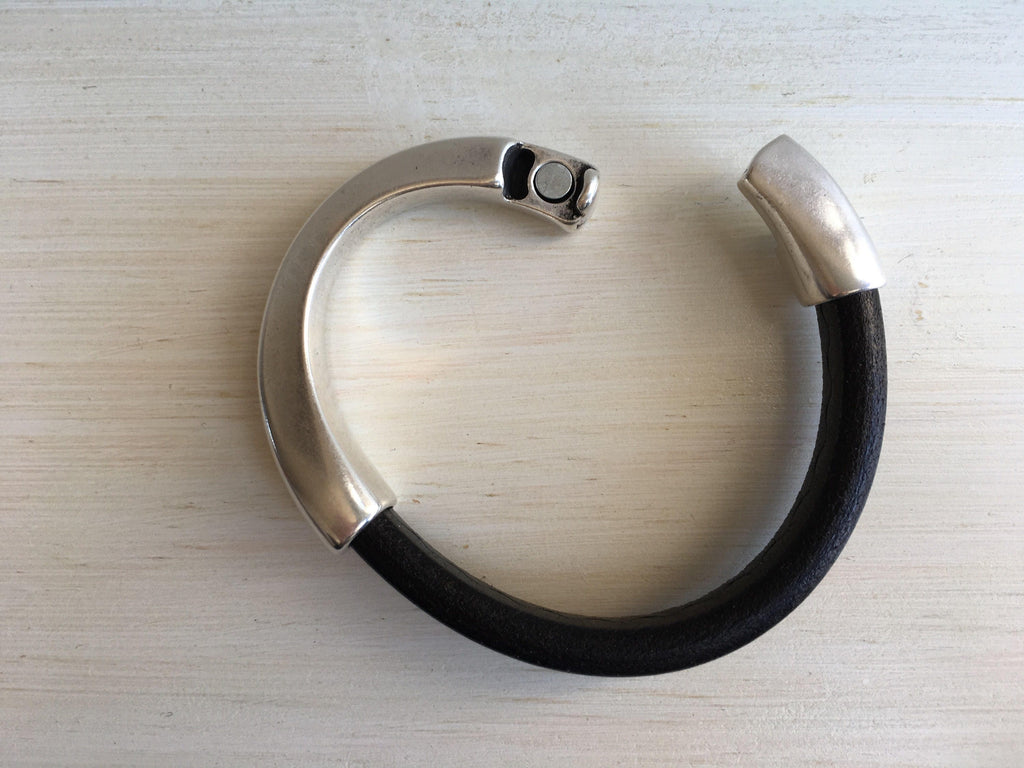 a thick black leather bracelet with silver clasp left open on a white table