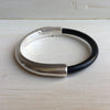 A black leather bracelet with silver clasp sits on a white table