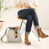 A woman wears jeans, leather boots and a gray braided leather bracelet with magnetic clasp while sitting in a chair