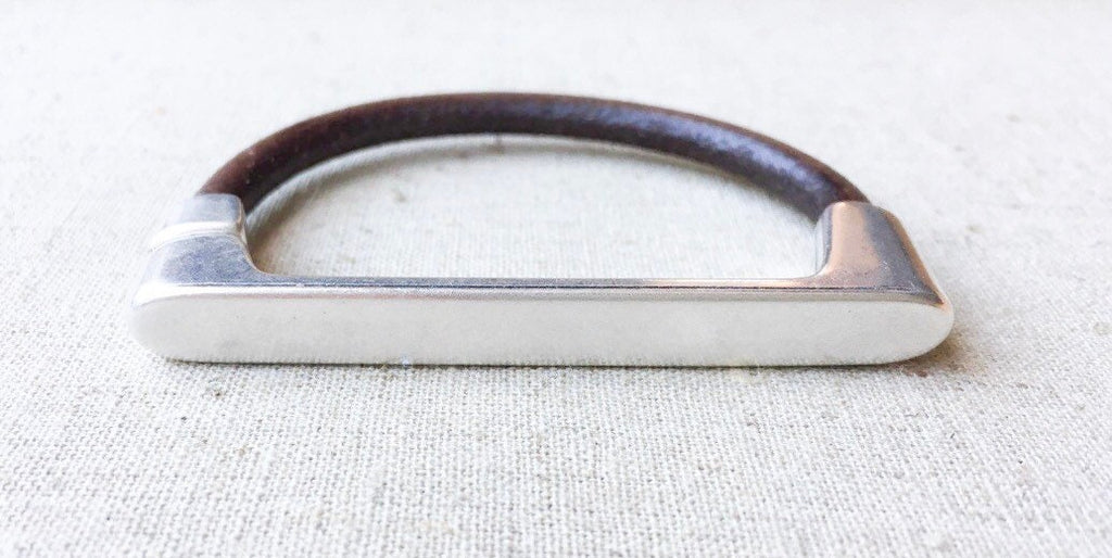 a brown leather and silver straight bar bracelet sits on a white cloth