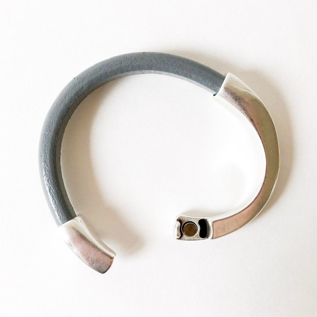A thick gray leather bracelet sits on a white table unclasped