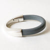 A thick gray leather bracelet sits on a white table