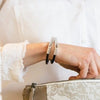 A thin black leather bracelet with silver straight bar clasp is worn on a woman's wrist