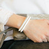 a woman wears a white shirt with black jeans and two thin black leather bracelets with silver straight bar clasps