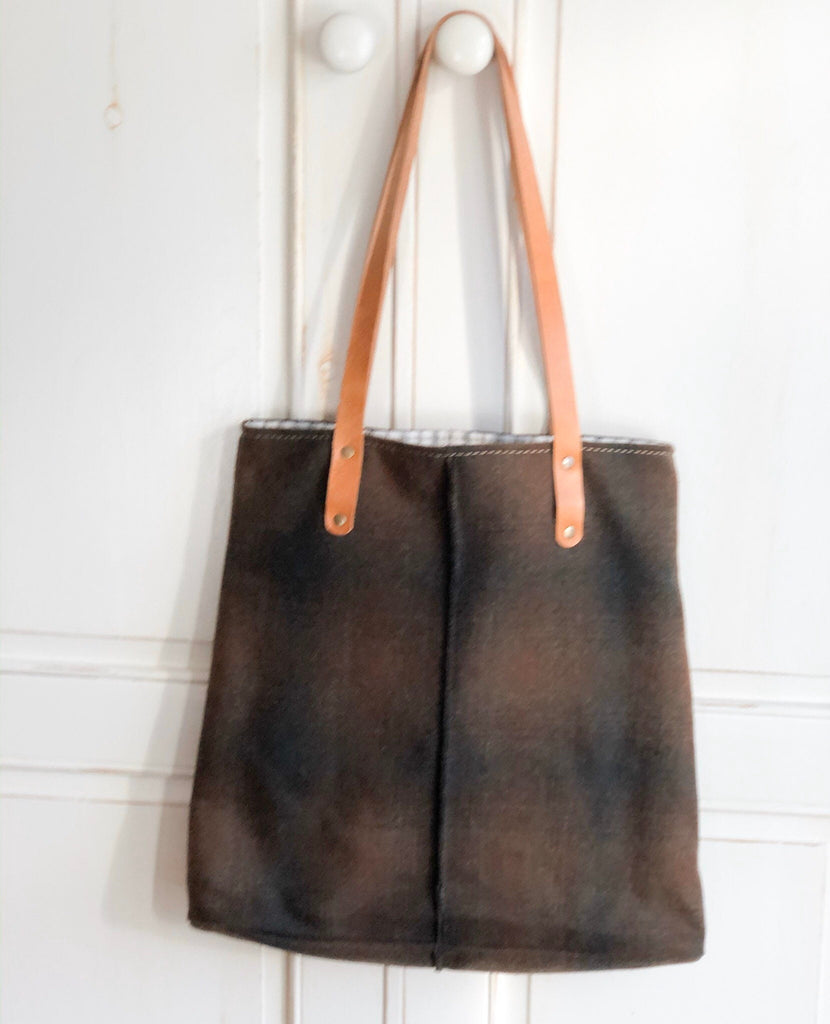 Gold Brown Plaid City Tote Felted Wool Bag with Handmade brown leather straps hangs on a white wooden door