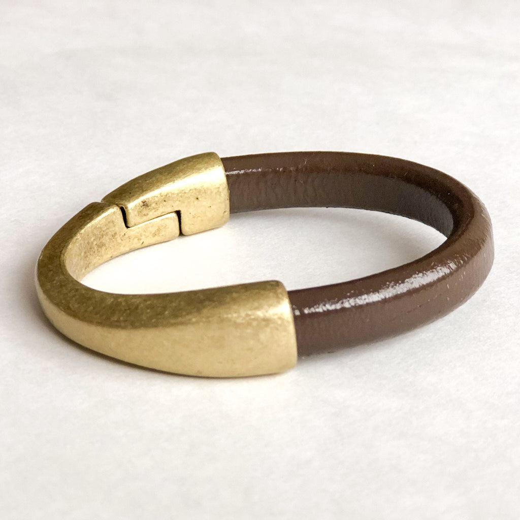 a cocoa brown leather cuff bracelet with antique brass clasp sits on a white table