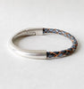 A gray metallic leather bracelet with silver clasp sits on a white table