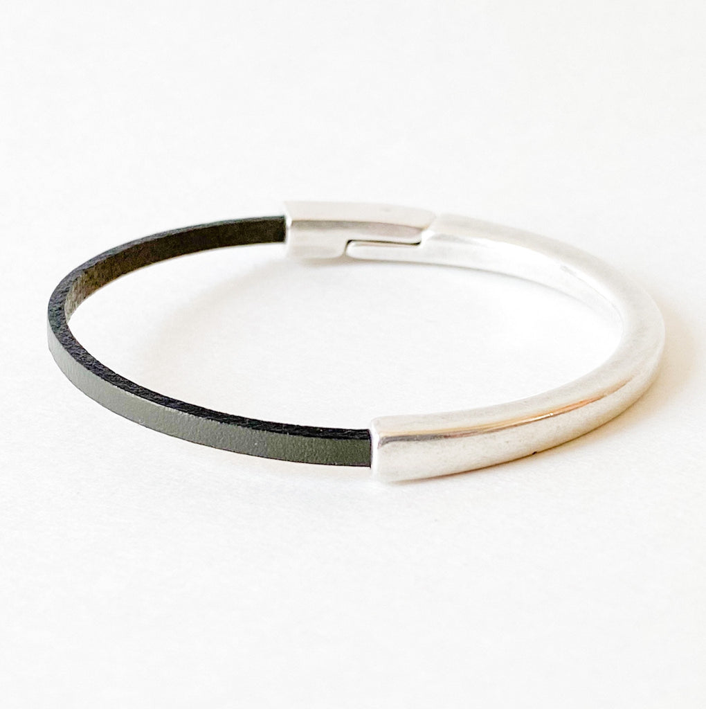 Aa dark gray thin leather bracelet with silver magnetic clasp on a white table