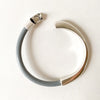 a thin gray leather bracelet with an opened silver half cuff clasp on a white table