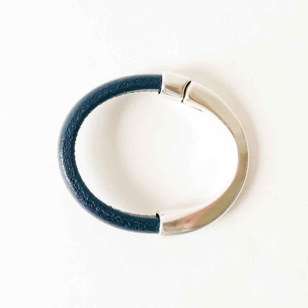 a women's navy leather bracelet with silver clasp sits on a white table