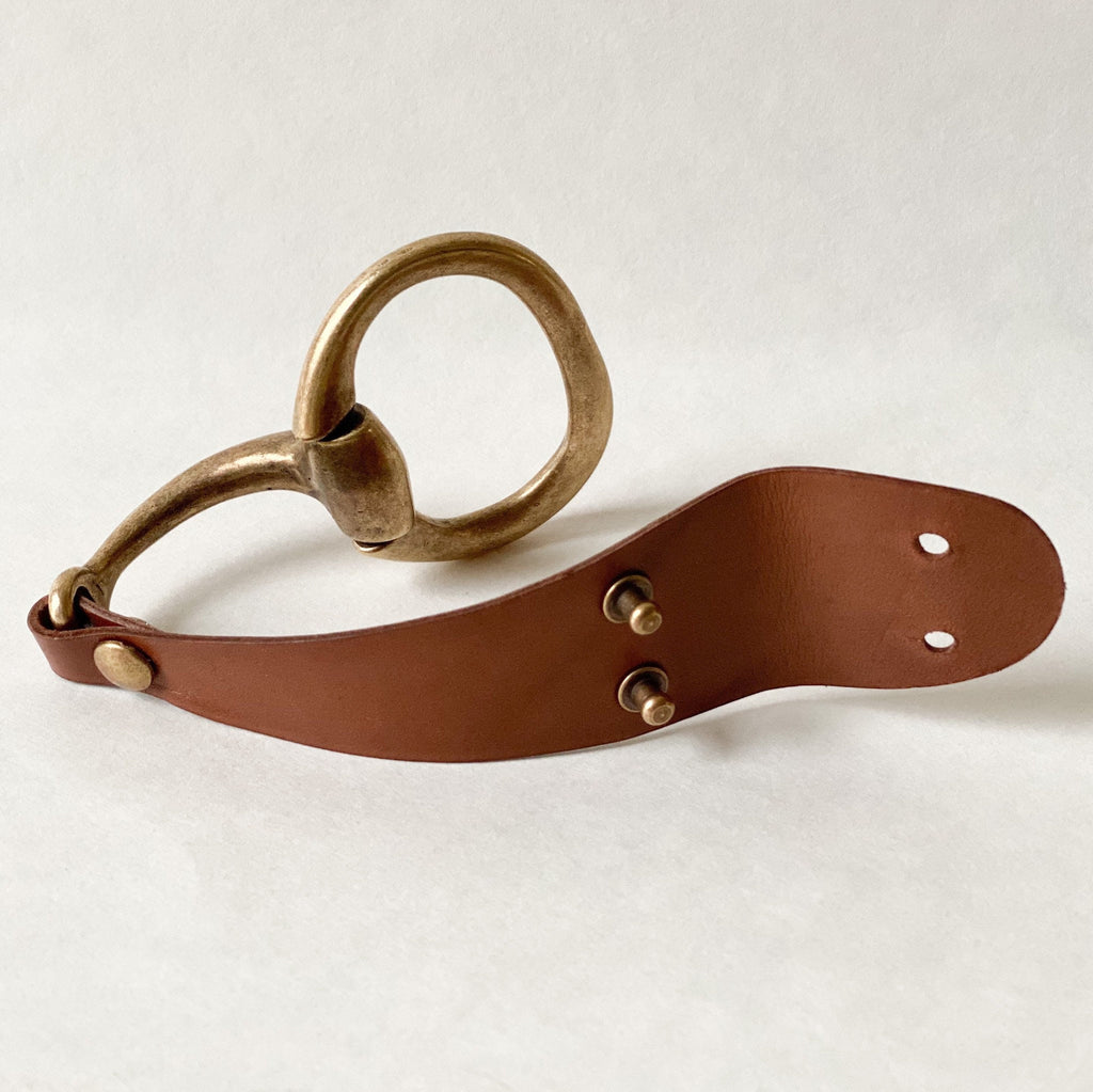 Large Antique Brass Snaffle Bit Bracelet with Brown Leather sits unclasped on a white table