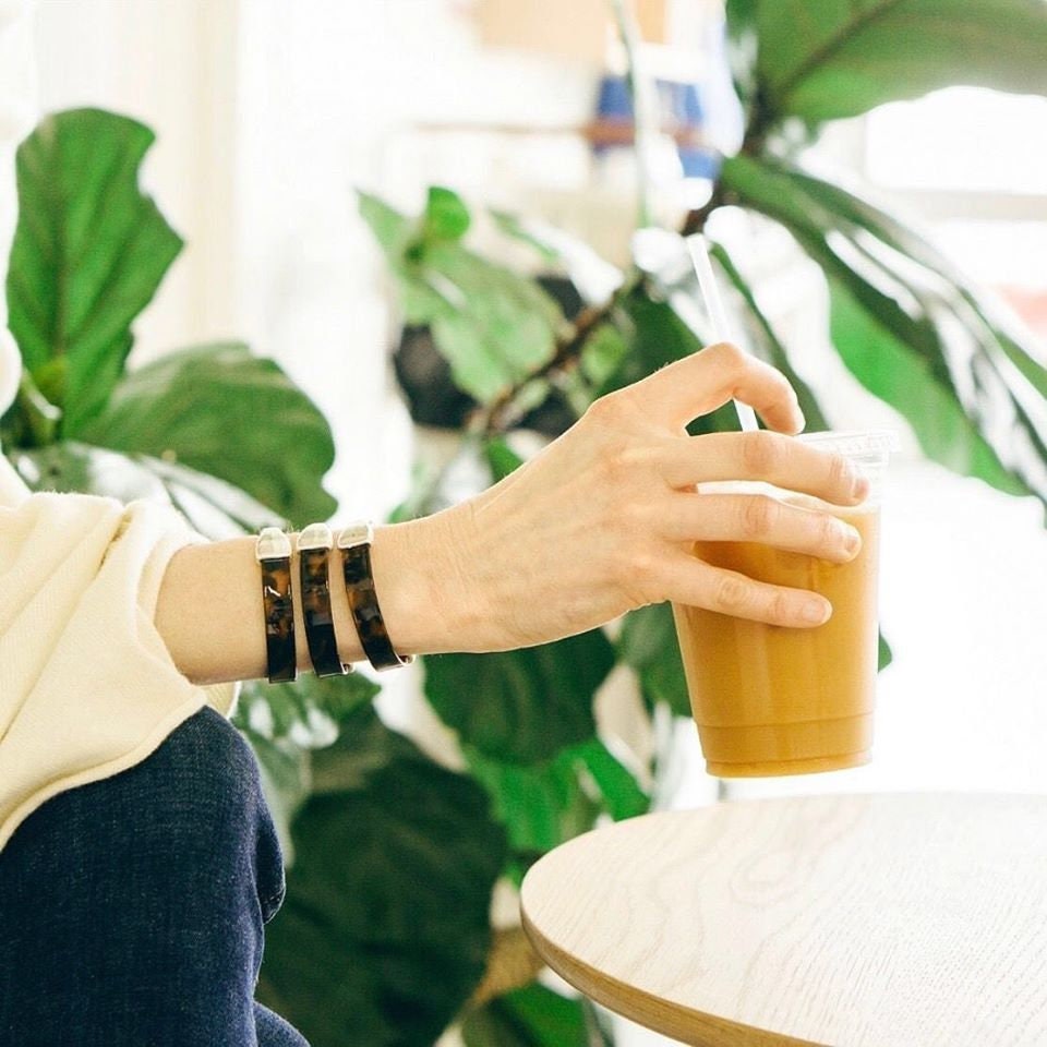 a woman wears three patent leather bracelets with silver clasps while holding an iced coffee