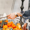 a women's navy leather bracelet is worn on a wrist carrying a basket off oranges