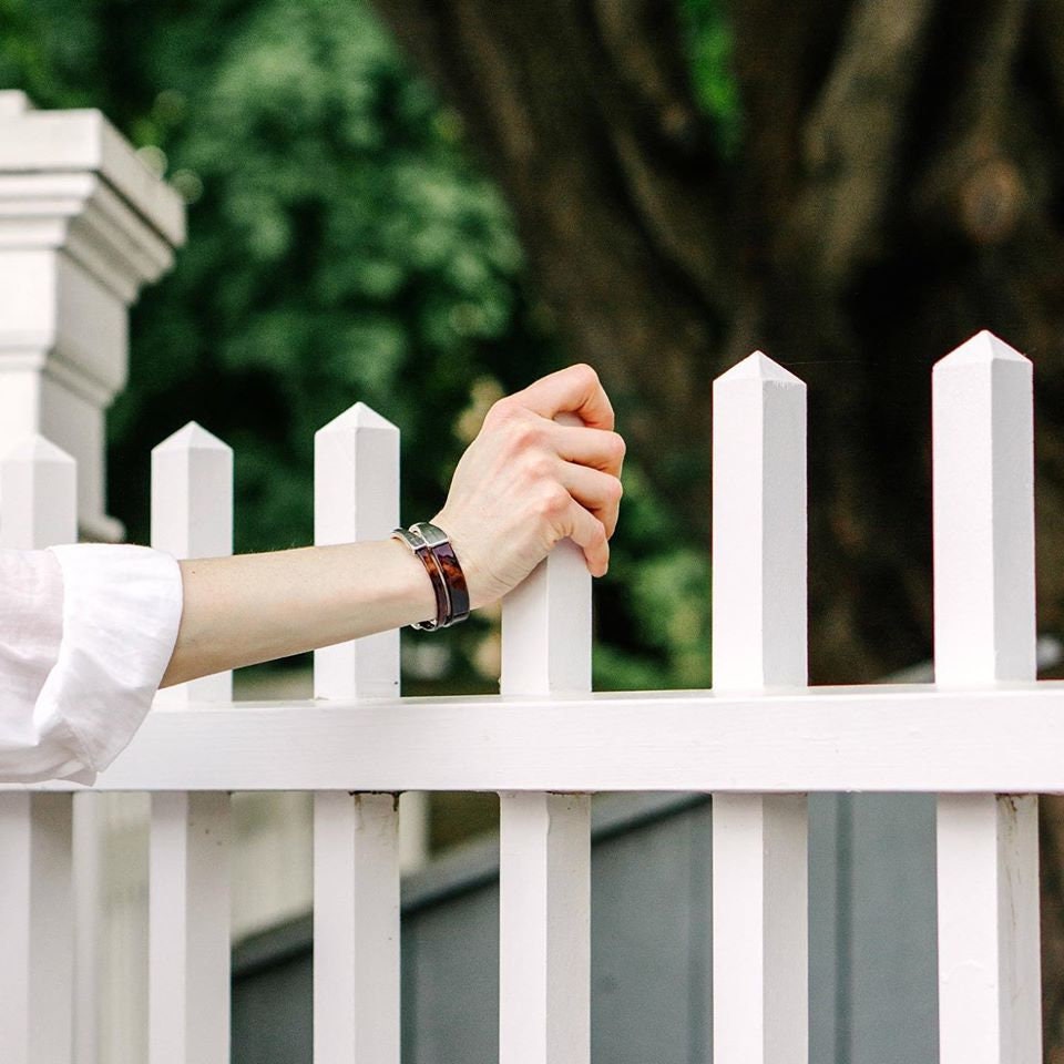 A woman wears a tortoise patent leather bracelet while holding on to a white picket fence