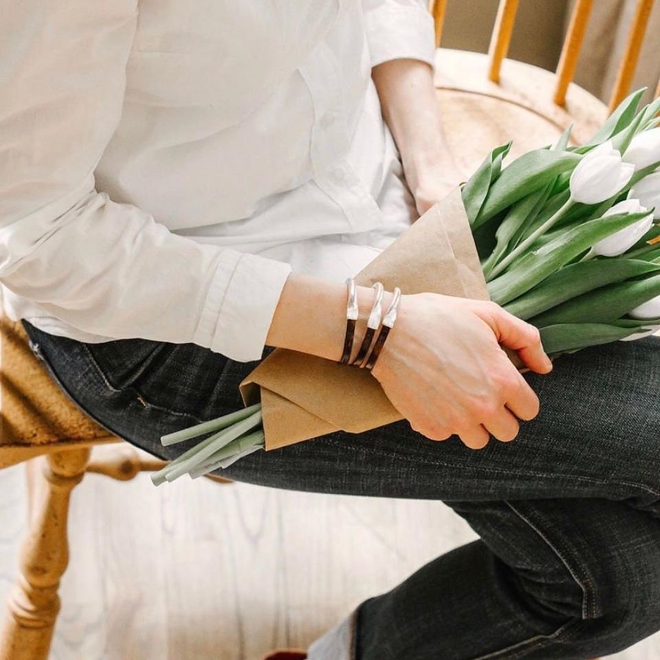 a woman wears three tortoise leather bracelets on her wrist while holding white tulips wrapped in brown paper
