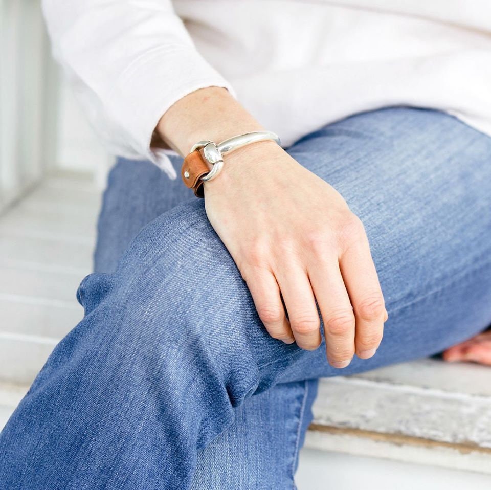 A woman wears an equestrian bracelet with light brown leather and silver snaffle bit