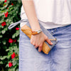 a woman wears a braided leather bracelet and thin leather bracelet  on her wrist with a denim skirt and white t-shirt