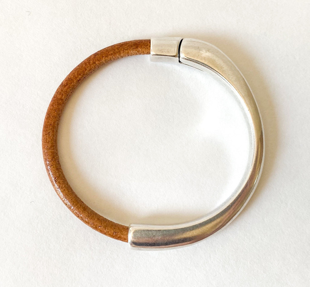 A camel  brown leather cuff bracelet with silver clasp sits on a white table