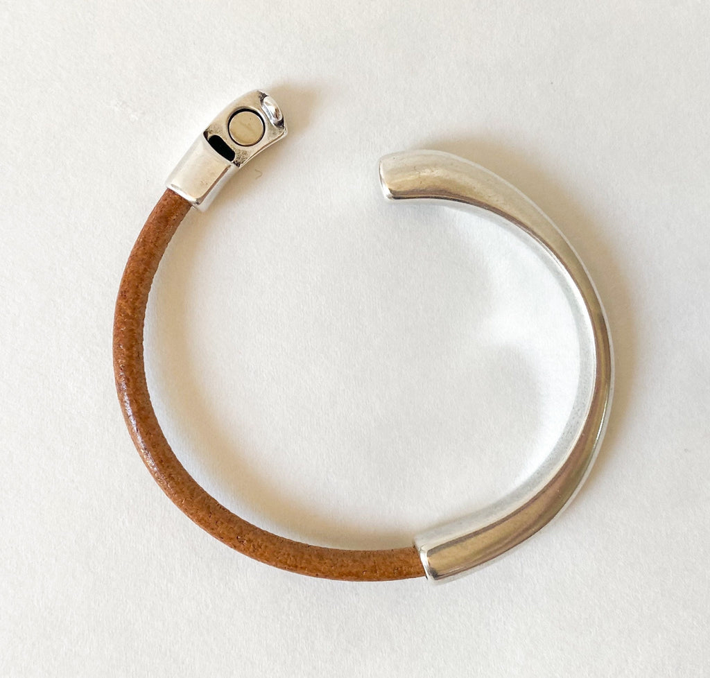 a cognac brown leather cuff bracelet with silver clasp undone on a white table