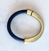 a dark navy blue leather bracelet with antique brass clasp on a white table