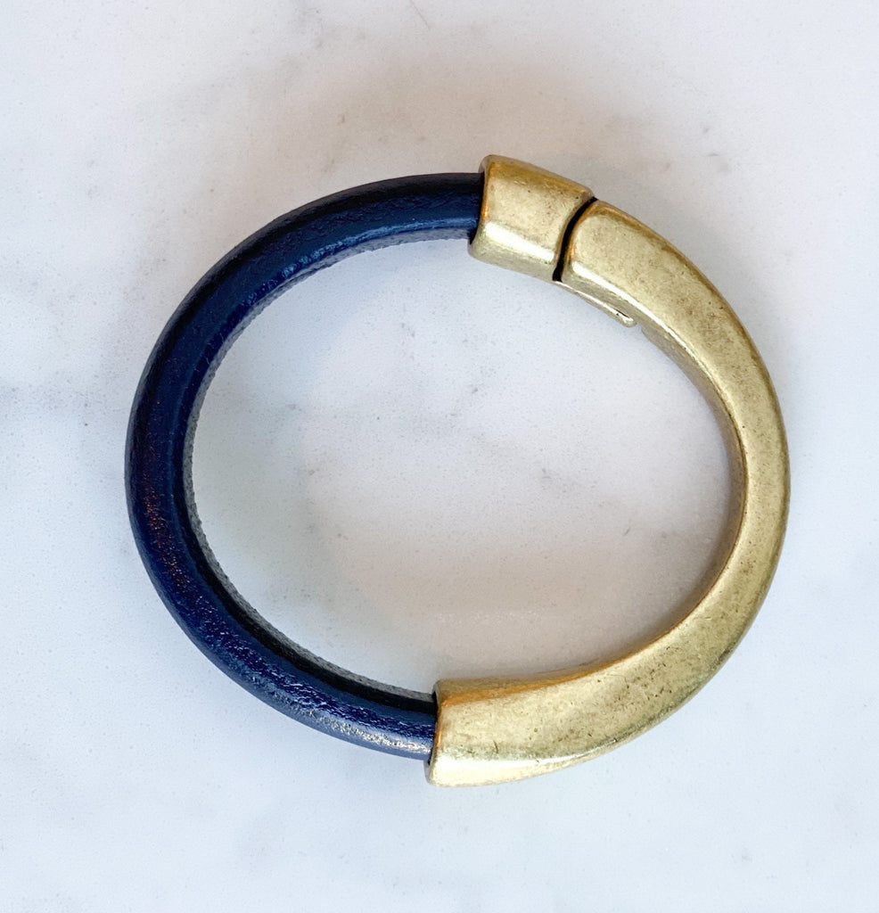 a dark navy blue leather bracelet with antique brass clasp on a white table