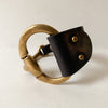 Large black leather and antique brass snaffle bit cuff on a white table