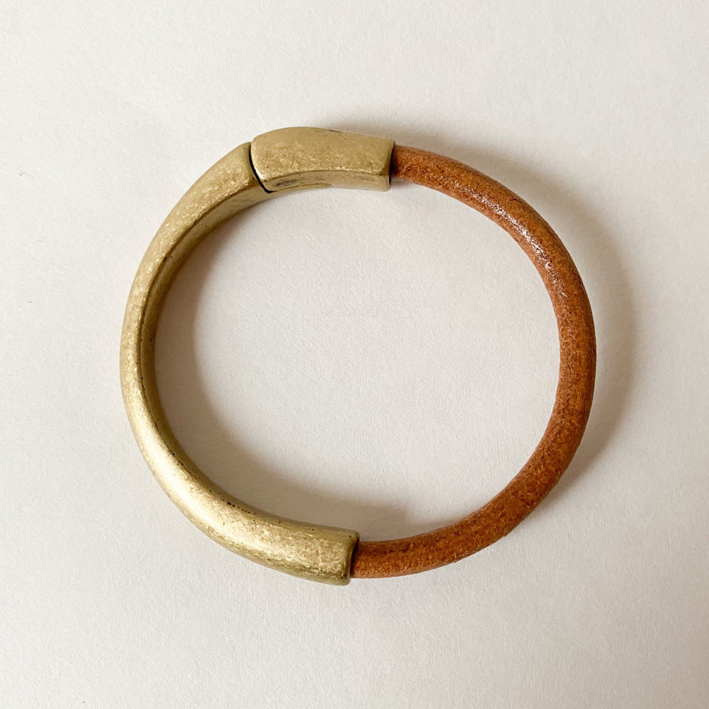 A light brown leather bracelet with antique brass clasp sits on a white table