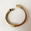 A light brown leather bracelet with antique brass clasp sits unclasped on a white table