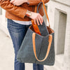 a woman wears a large snaffle bit bracelet with brown leather while wearing a brown leather jacket and holding a striped tote bag