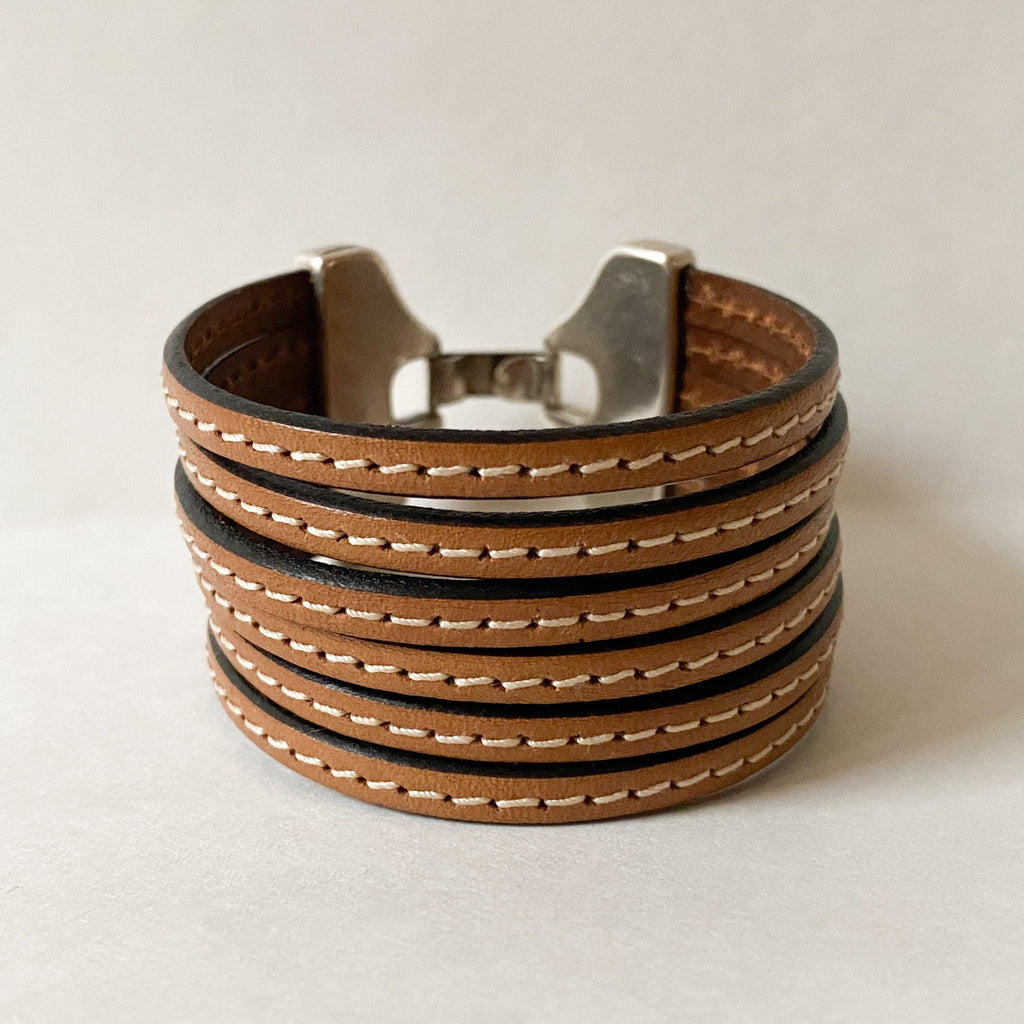 a camel brown leather multi strand cuff bracelet sits on a white table with leather strands facing forward