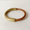 A light brown leather bracelet with antique brass magnetic clasp sits on a white table