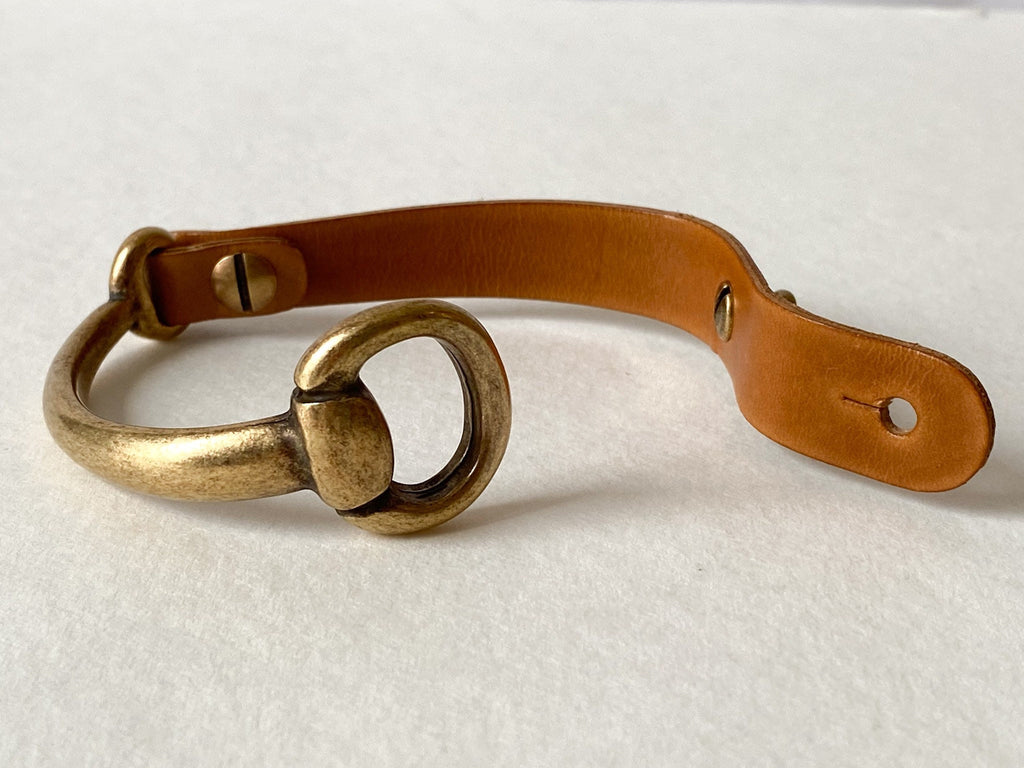 An antique brass and brown leather small snaffle bit with undone clasp