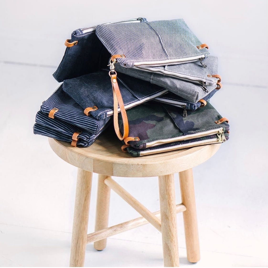 A stack of crossbody pouch bags sits on a wooden stool
