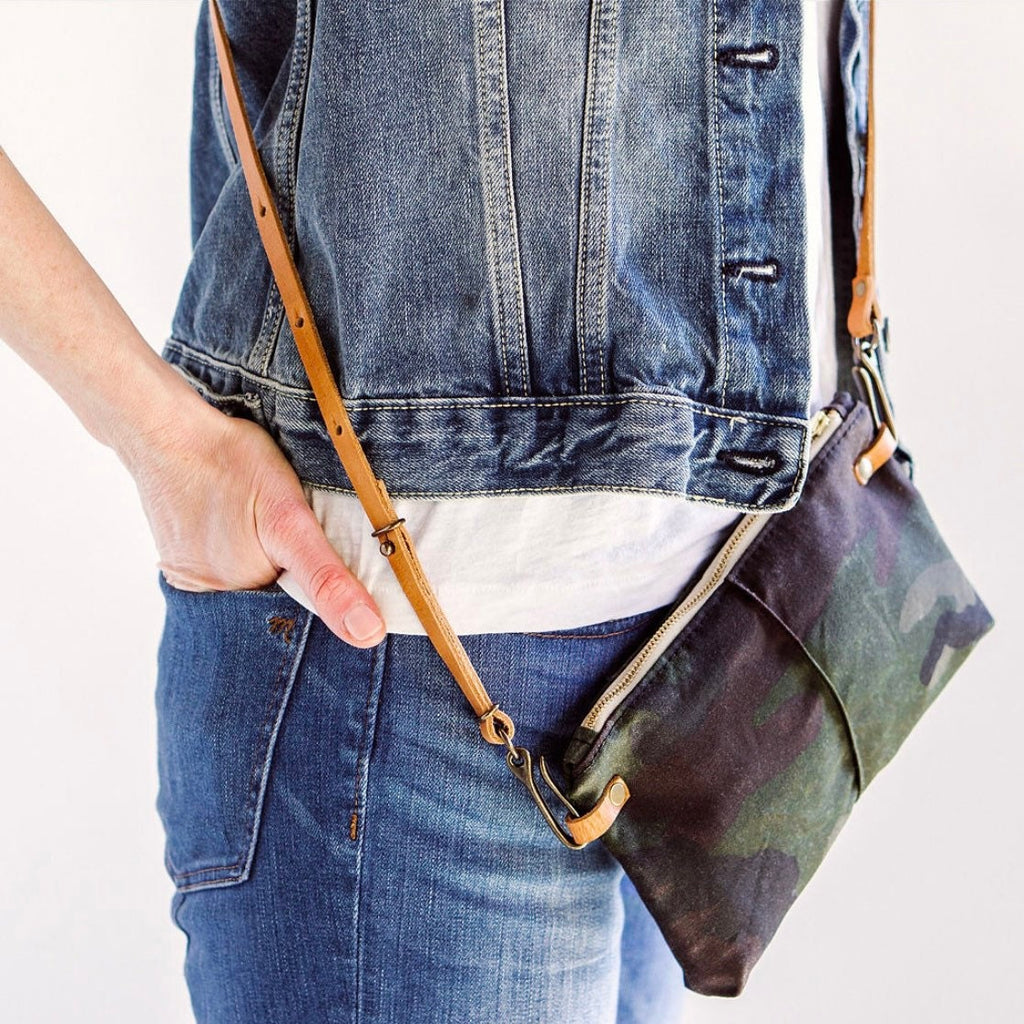 a leather crossbody strap is attached to a camouflage wristlet pouch