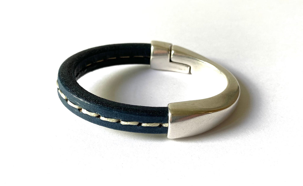 a dark navy leather bracelet with white stitching and silver magnetic clasp on a white table