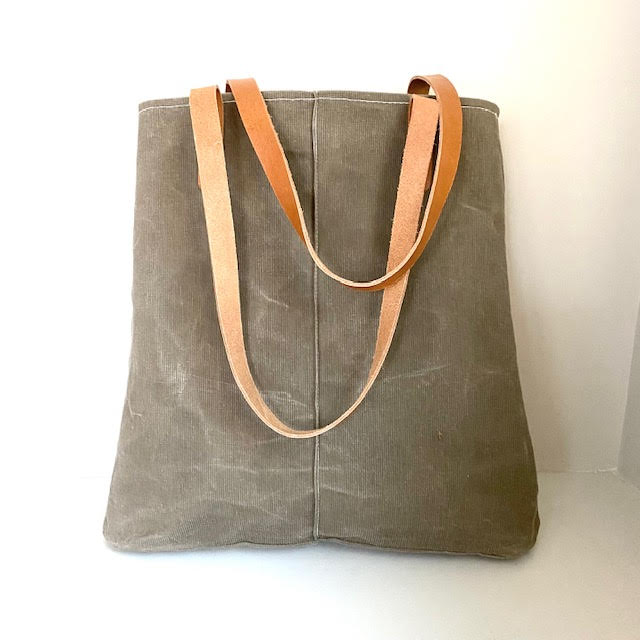 A beige waxed corduroy tote bag with brown leather straps